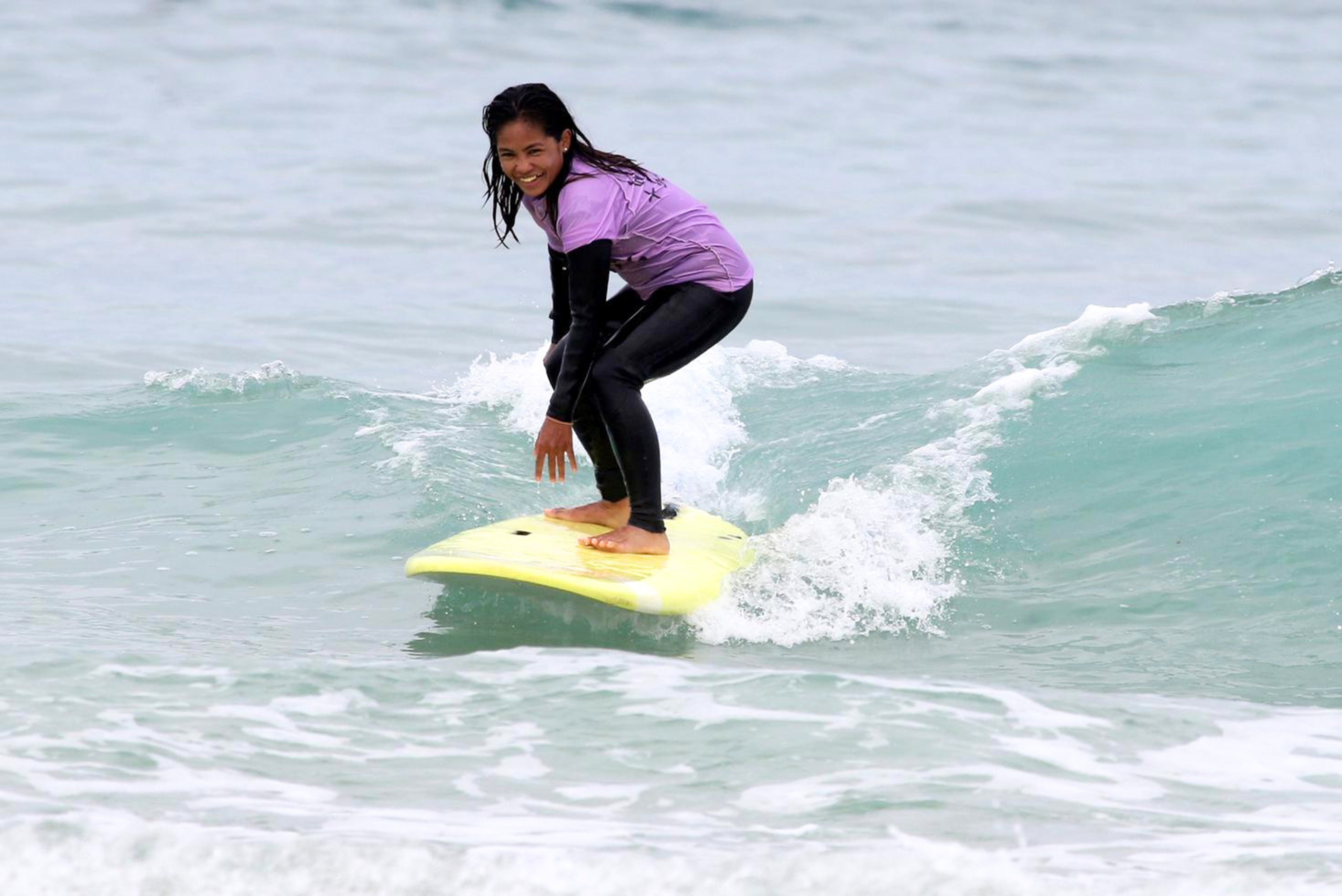 Woman standing up on a surfboard catching a wave for the first time at Newquay beach