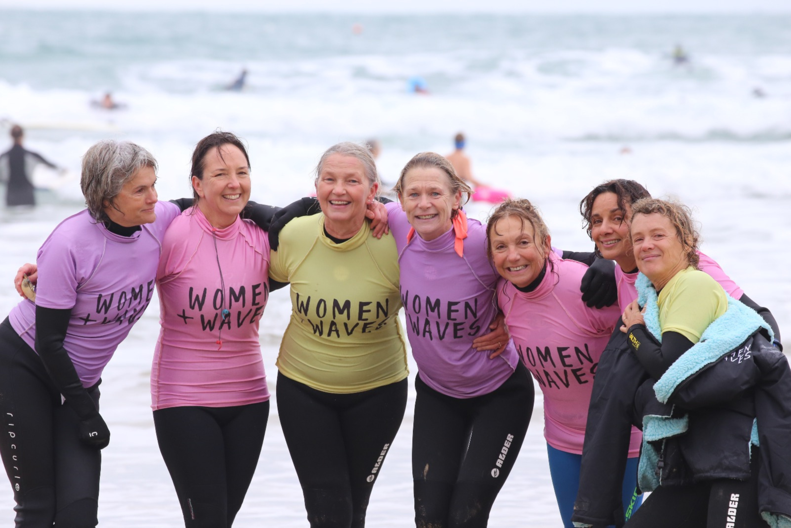 Group of smiling women on Newquay beach after surfing at Women and Waves Cornwall