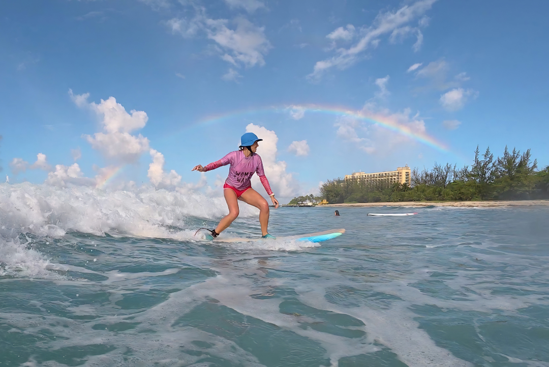 Woman over 40 surfing in Barbados under rainbow.