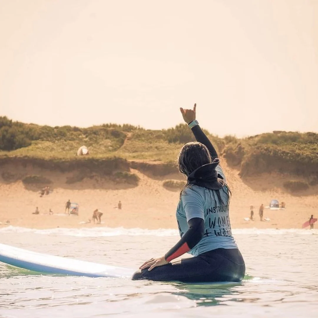 Girl on surfboard doing a Shakka with her hand